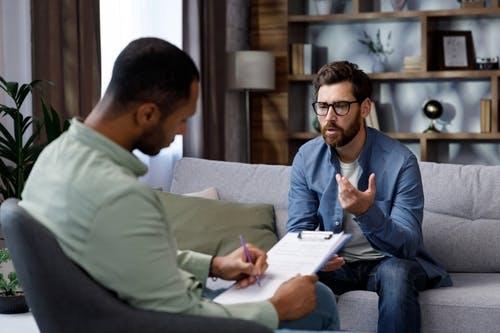  A man sits on a couch and talks to a psychotherapist. The patient is depressed, apathetic and stressed from problems in his personal life. 