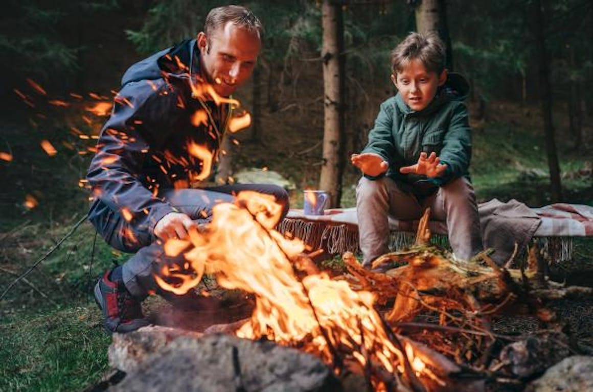 A man camping with his son by a campfire